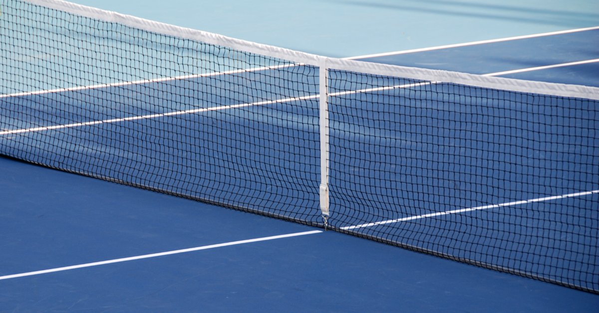 A Guide to Choosing the Right Tennis Net for Your Court A tennis net spanning a blue court with a white center strap, white border lines, and a lighter blue court area beyond it.