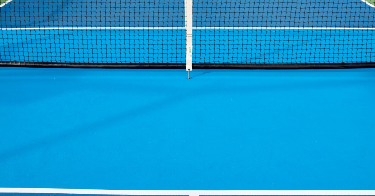 A close-up view of a pickleball net stretched across a blue court with clear white lines and a clean playing surface.