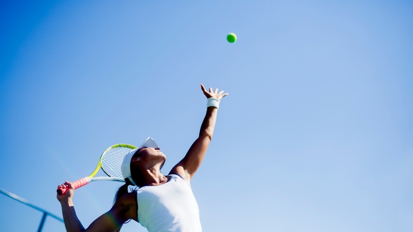  A woman wearing a white hat and a top attempts to serve a tennis ball with her right hand during the day.
