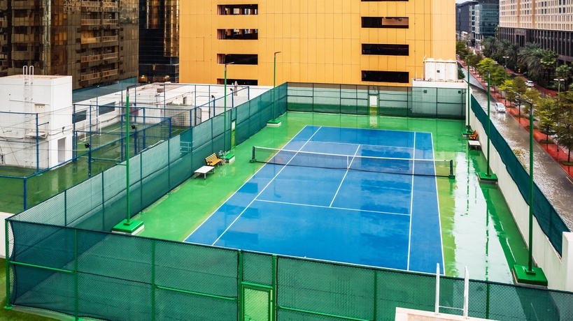 A tennis court located in the middle of an urban area on a rainy day, causing standing water on the court and the streets.