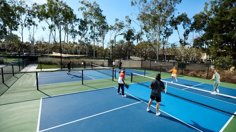 Four people are playing pickleball on a court with a light blue forecourt and dark blue backcourt. Four people are playing pickleball on a court with a light blue forecourt and dark blue backcourt.